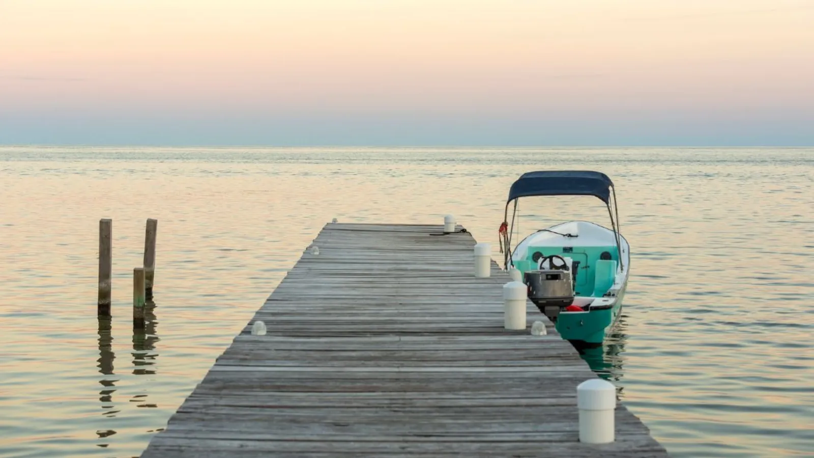 A wooden pier running out over calm water at dawn, with a small boat moored alongside.